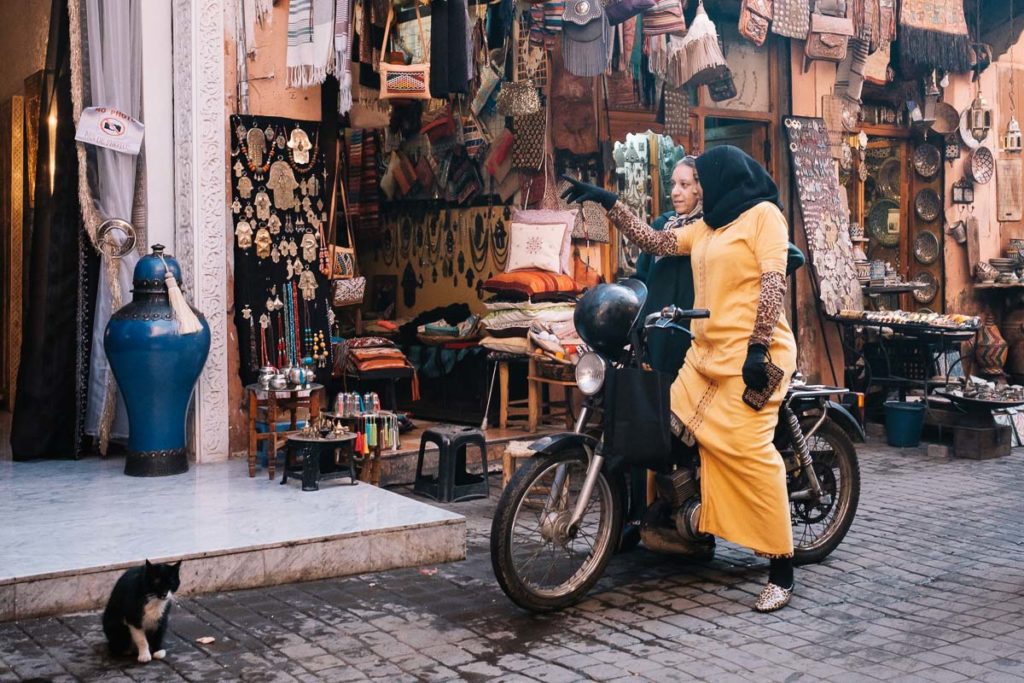 Moderne und Tradition treffen aufeinander in Marrakesch. Eine Frau in traditioneller Kleidung fährt mit dem Moped zum Einkaufen.