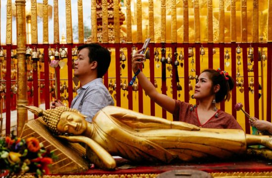 Beten und Selfies: Besucher des Wat Phra That Doi Suthep beten nach vorgegebenen Ritual oder machen Fotos von sich und dem Temepl. Im Vordergrund eine liegende Buddha-Statue