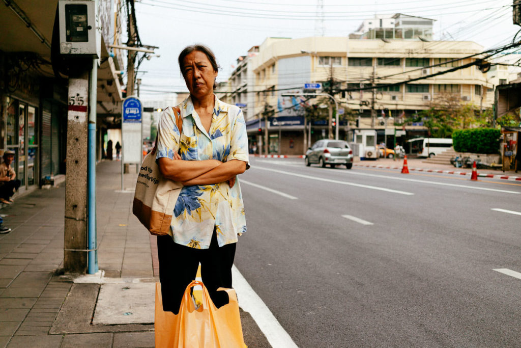 Frau wartet mit ihren Einkäufen am Straßenrand