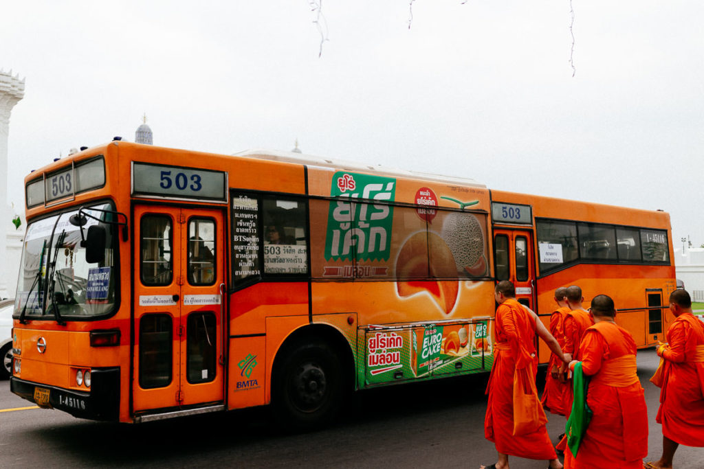 Nahe des Großen Palastes in Bangkok überqueren ein Bus und Mönche eine Straße