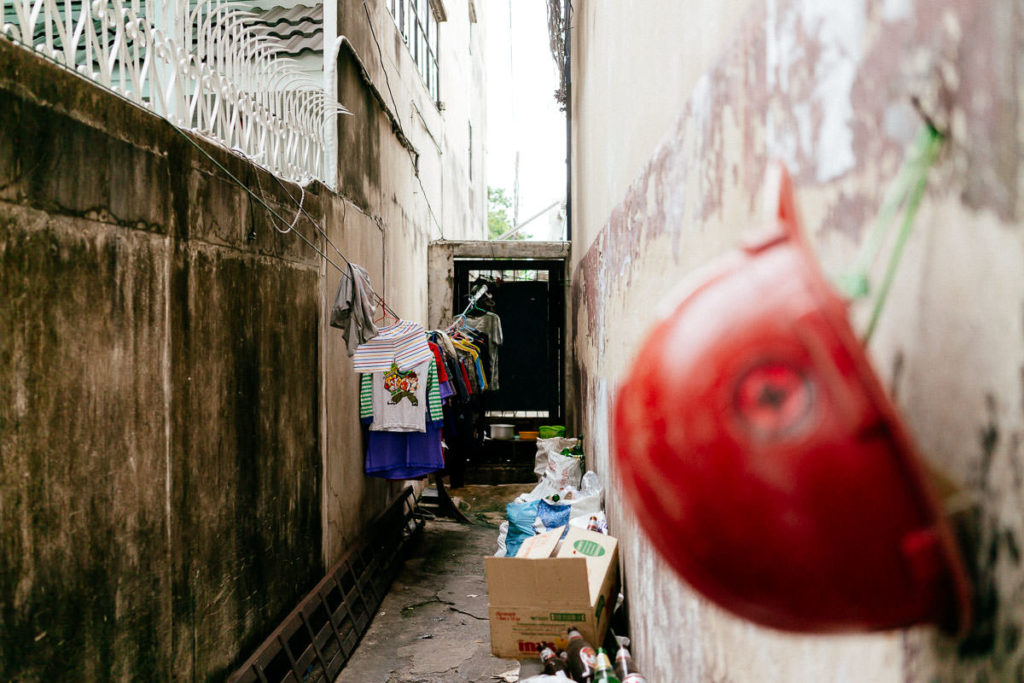 Blick in schmale Gasse in Bangkok mit Gerümpel, im Vordergrund ein roter Helm