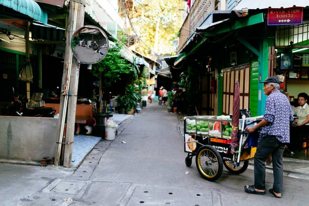 Ein Obstverkäufer geht mit seinem mobilen Verkaufsstand durch die Gassen in Talat Noi, Bangkok