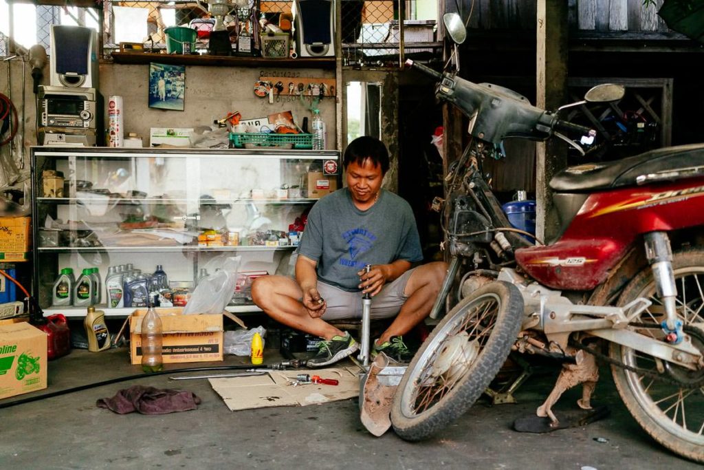 Kleine Werkstatt in Chiang Mai. Handwerker und Motorrad teilen sich wenige Quadratmeter