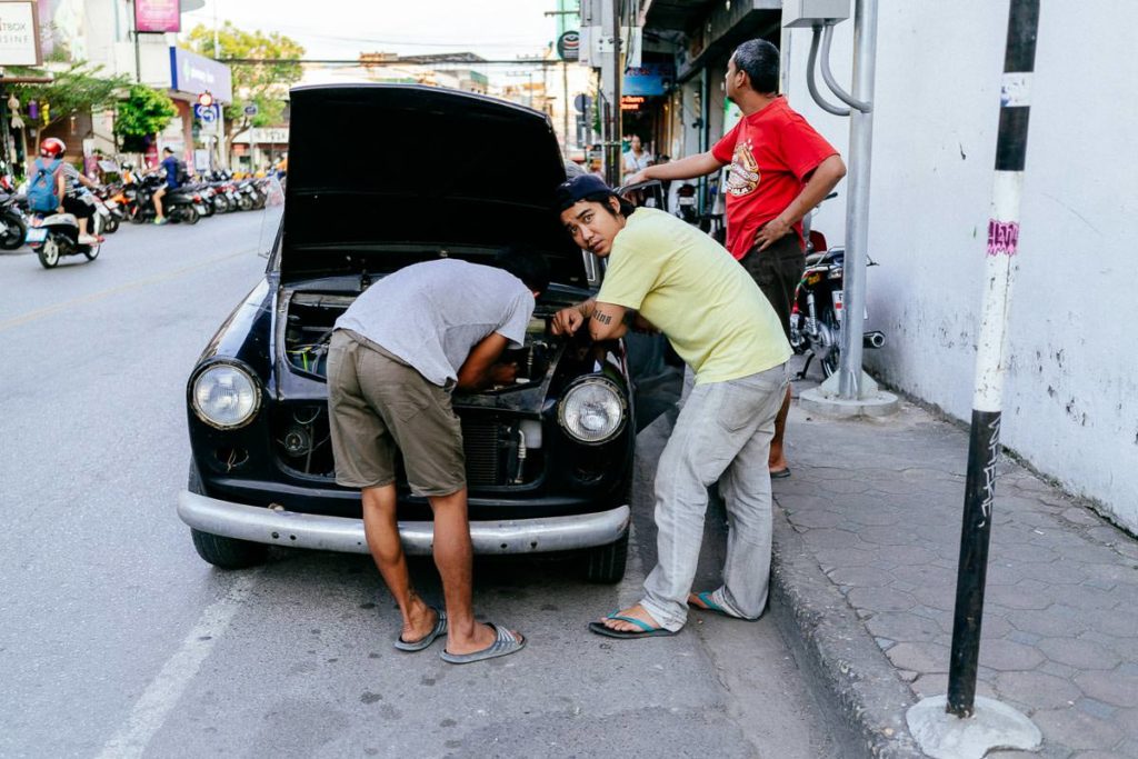 Zwei Männer basteln auf der Straße am Oldtimer